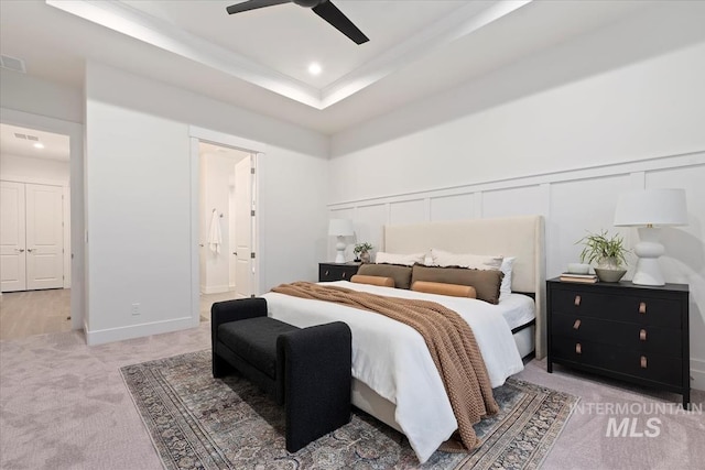 bedroom featuring ceiling fan, ensuite bath, a raised ceiling, and light carpet