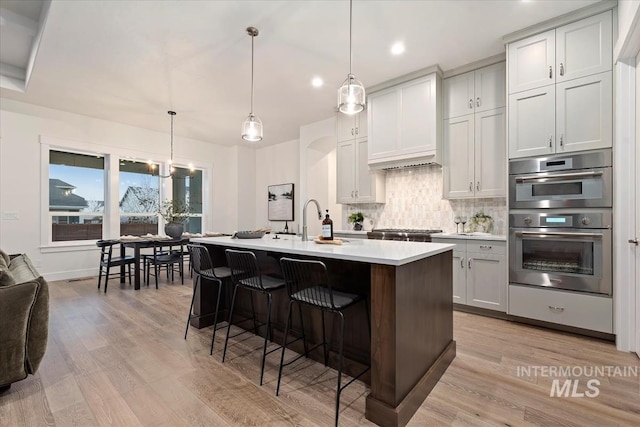 kitchen featuring a center island with sink, hanging light fixtures, a breakfast bar, light hardwood / wood-style flooring, and decorative backsplash