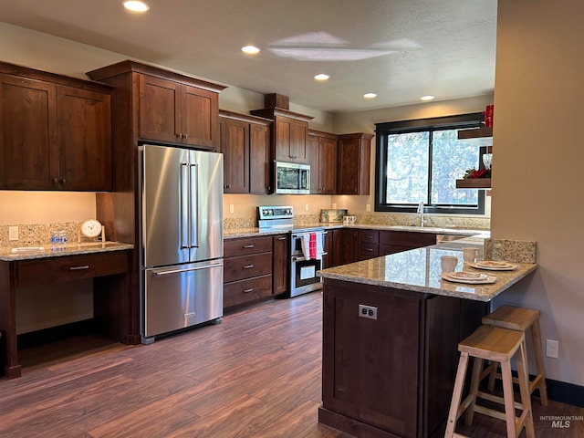 kitchen with light stone countertops, dark hardwood / wood-style flooring, kitchen peninsula, stainless steel appliances, and a breakfast bar area