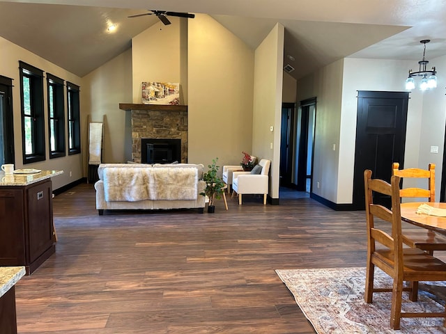 living room with ceiling fan with notable chandelier, dark hardwood / wood-style flooring, vaulted ceiling, and a fireplace