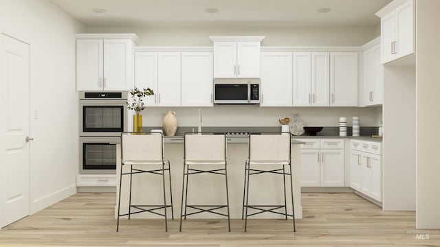 kitchen featuring a kitchen bar, light wood-type flooring, stainless steel appliances, and white cabinetry