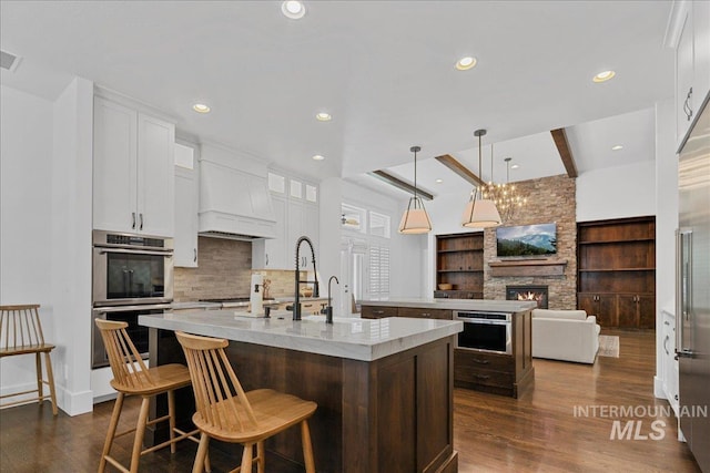 3345 W Dublin St, Eagle, ID 83616 - kitchen with stainless steel double oven, a kitchen island with sink, a fireplace, backsplash, and dark wood finished floors