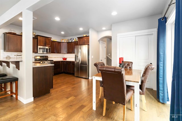 kitchen with arched walkways, light wood-style flooring, appliances with stainless steel finishes, a peninsula, and recessed lighting