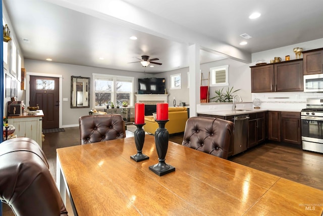 kitchen with light countertops, appliances with stainless steel finishes, open floor plan, a sink, and dark brown cabinetry