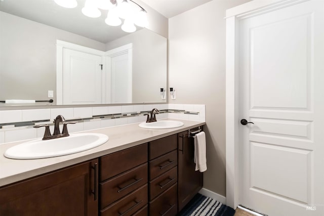 bathroom with baseboards, double vanity, a sink, and decorative backsplash