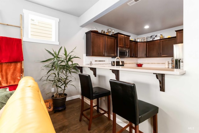 kitchen featuring dark wood-style floors, appliances with stainless steel finishes, light countertops, and a breakfast bar area