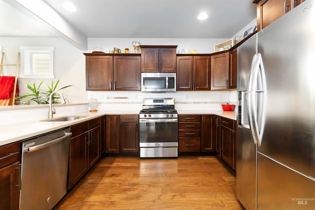 kitchen featuring stainless steel appliances, wood finished floors, a sink, light countertops, and tasteful backsplash