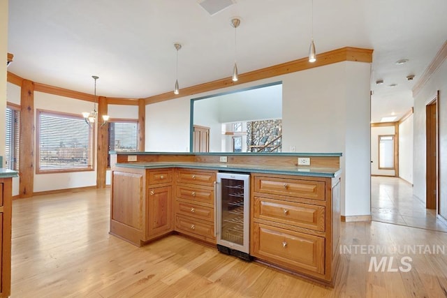 kitchen with crown molding, decorative light fixtures, light wood-type flooring, a notable chandelier, and beverage cooler