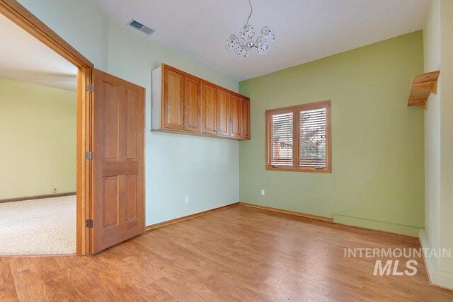 spare room featuring light wood-type flooring and a notable chandelier