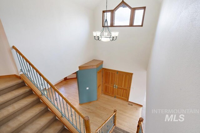 stairway featuring wood-type flooring, a high ceiling, and an inviting chandelier