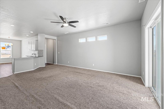 unfurnished living room with plenty of natural light, carpet flooring, and ceiling fan with notable chandelier