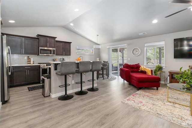 kitchen with appliances with stainless steel finishes, vaulted ceiling, healthy amount of natural light, light countertops, and a breakfast bar