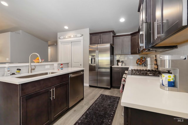 kitchen with appliances with stainless steel finishes, a sink, dark brown cabinets, decorative backsplash, and light wood finished floors