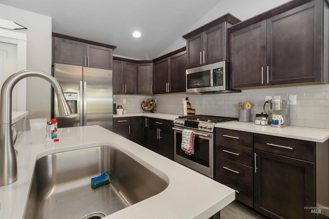 kitchen featuring stainless steel appliances, a sink, light countertops, tasteful backsplash, and vaulted ceiling