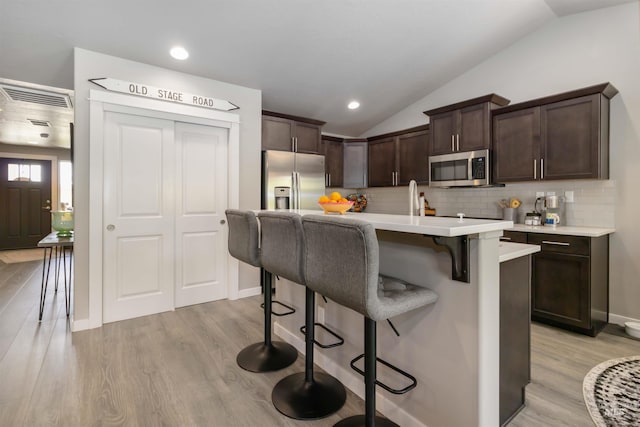kitchen featuring appliances with stainless steel finishes, a kitchen breakfast bar, dark brown cabinetry, lofted ceiling, and light countertops