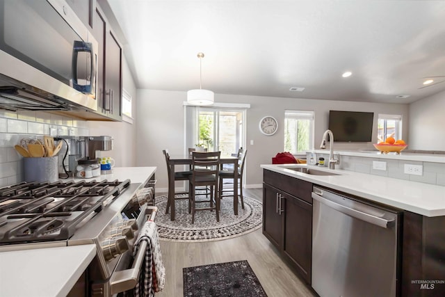 kitchen featuring stainless steel appliances, a sink, light wood-type flooring, light countertops, and dark brown cabinets