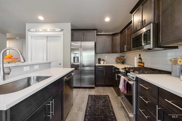 kitchen featuring stainless steel appliances, a sink, light countertops, dark brown cabinets, and tasteful backsplash