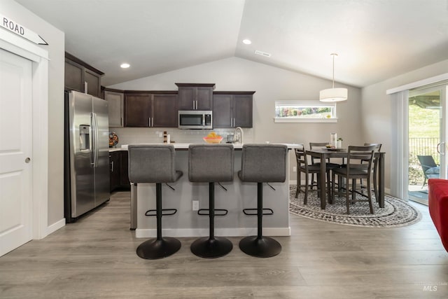 kitchen with stainless steel appliances, lofted ceiling, light wood finished floors, dark brown cabinetry, and light countertops