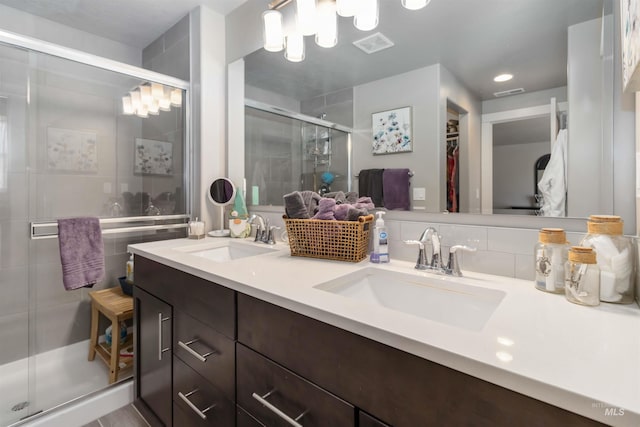 bathroom featuring a shower stall, double vanity, and a walk in closet