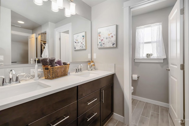 full bath featuring toilet, baseboards, double vanity, a spacious closet, and recessed lighting