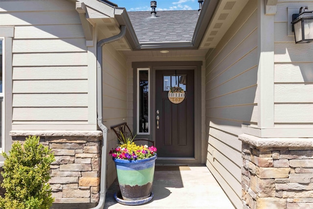 entrance to property featuring stone siding and a shingled roof