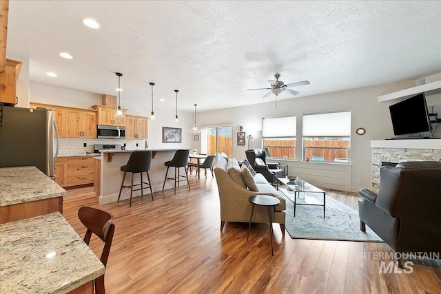 living room featuring recessed lighting, a textured ceiling, light wood-type flooring, and a ceiling fan