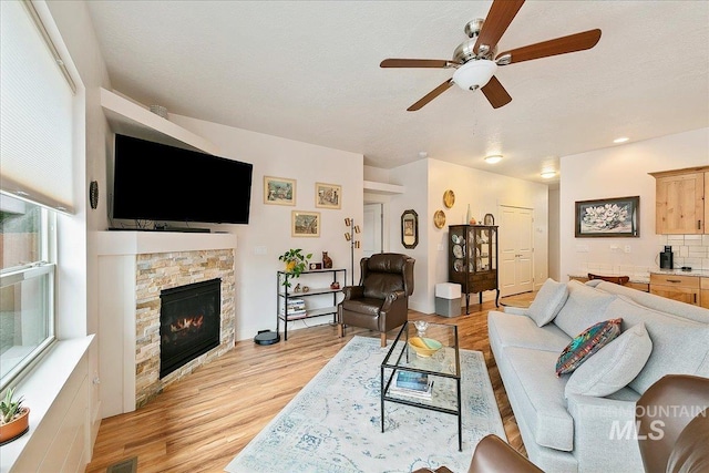 living area featuring a ceiling fan, a fireplace, visible vents, and light wood finished floors