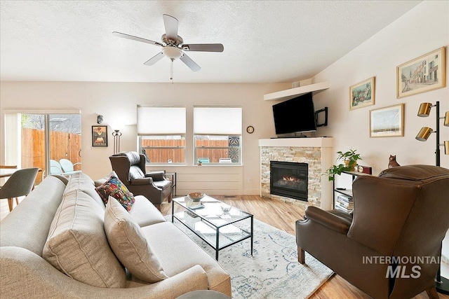 living area with a ceiling fan, a textured ceiling, wood finished floors, and a fireplace