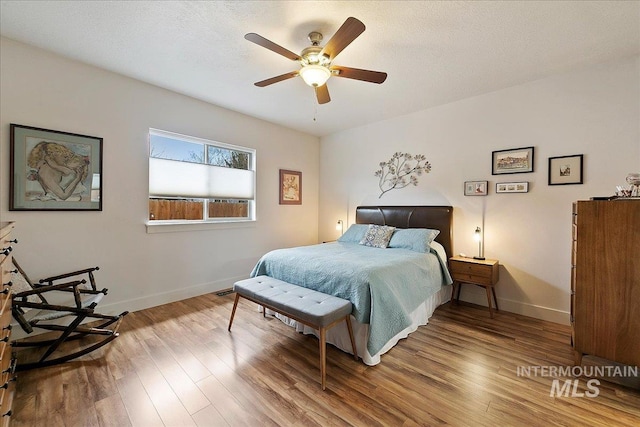 bedroom featuring ceiling fan, a textured ceiling, baseboards, and wood finished floors