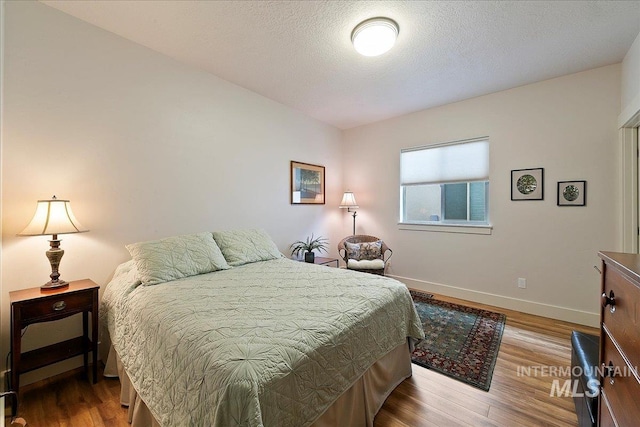 bedroom with baseboards, a textured ceiling, and wood finished floors