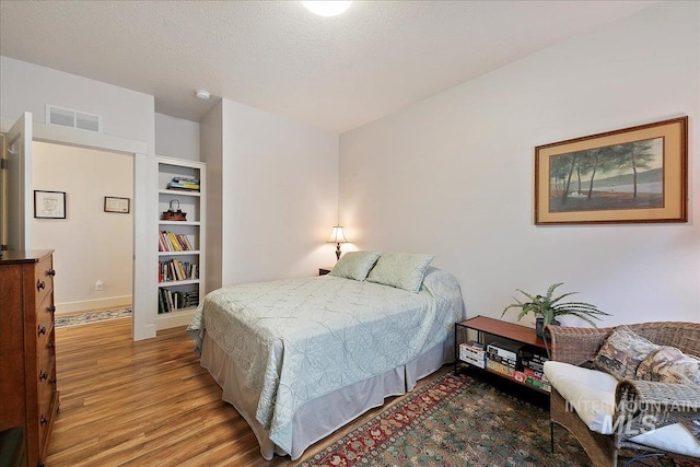 bedroom featuring visible vents, a textured ceiling, baseboards, and wood finished floors