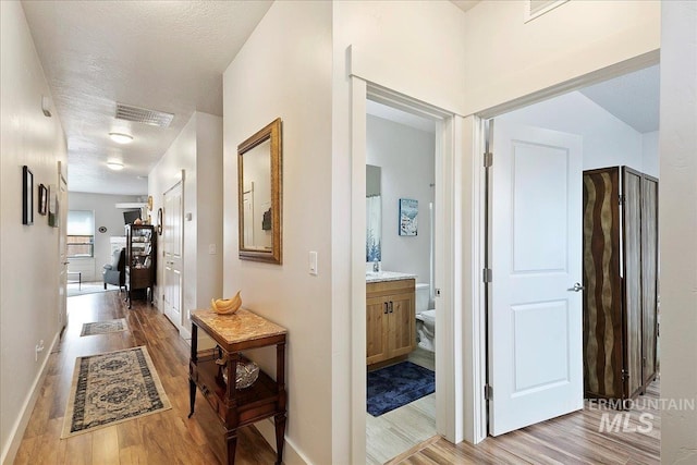 hallway with baseboards, visible vents, a textured ceiling, and light wood-style floors