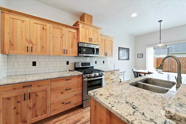 kitchen featuring light wood-style flooring, a sink, light brown cabinetry, stainless steel appliances, and tasteful backsplash