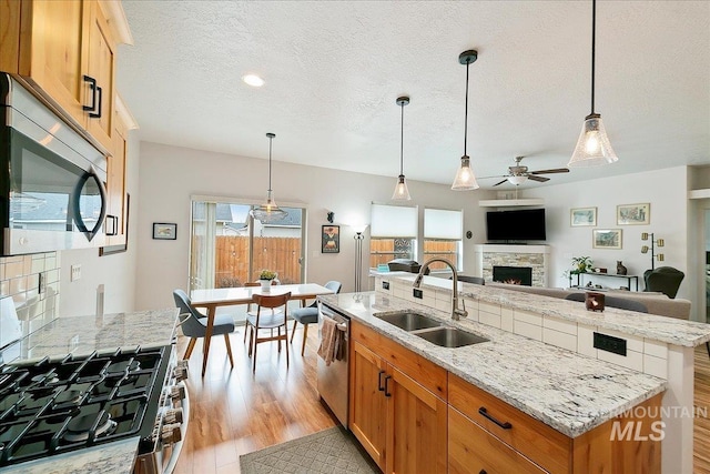 kitchen with light wood finished floors, a sink, appliances with stainless steel finishes, a fireplace, and a kitchen island with sink