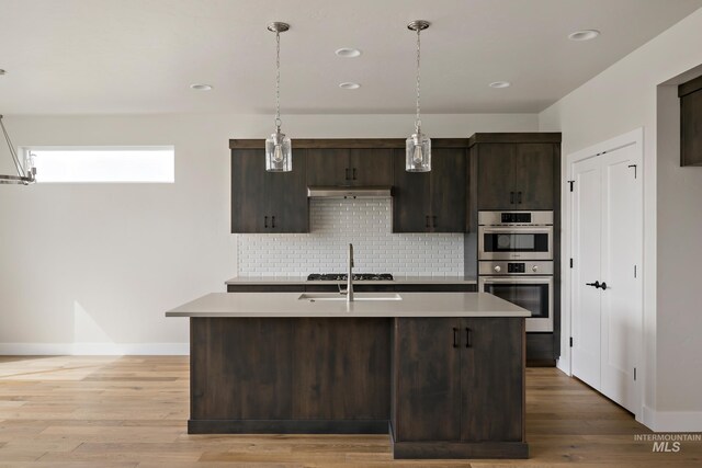 kitchen featuring wood-type flooring, a kitchen island with sink, dark brown cabinets, and decorative light fixtures