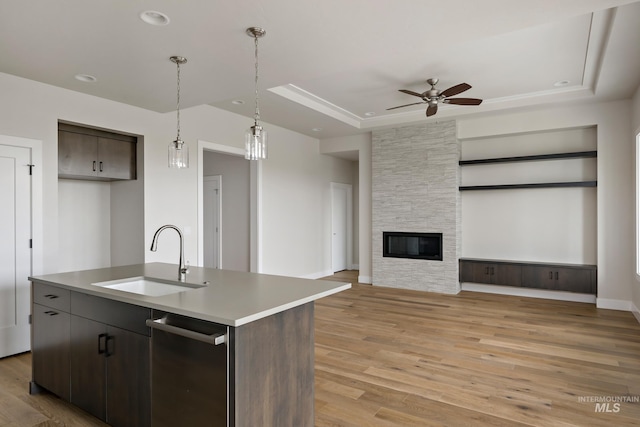 kitchen with dark brown cabinets, light hardwood / wood-style floors, sink, an island with sink, and a raised ceiling