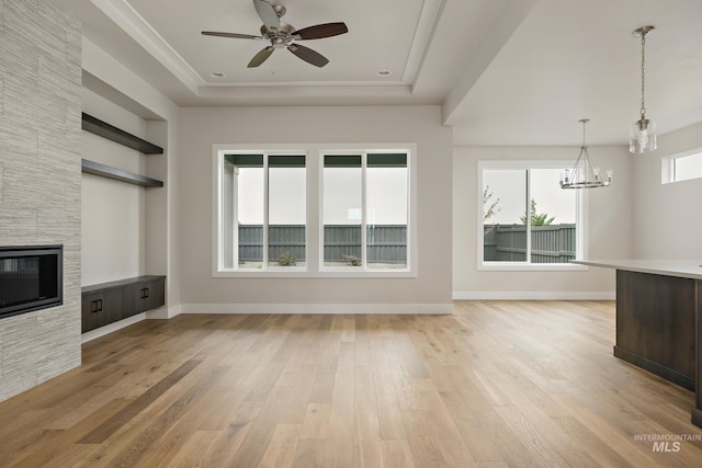 unfurnished living room featuring ceiling fan with notable chandelier, a stone fireplace, light hardwood / wood-style flooring, and a wealth of natural light