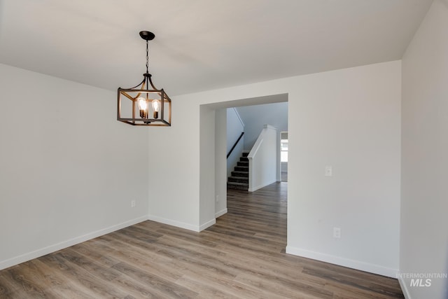 unfurnished room with stairway, a notable chandelier, baseboards, and light wood finished floors