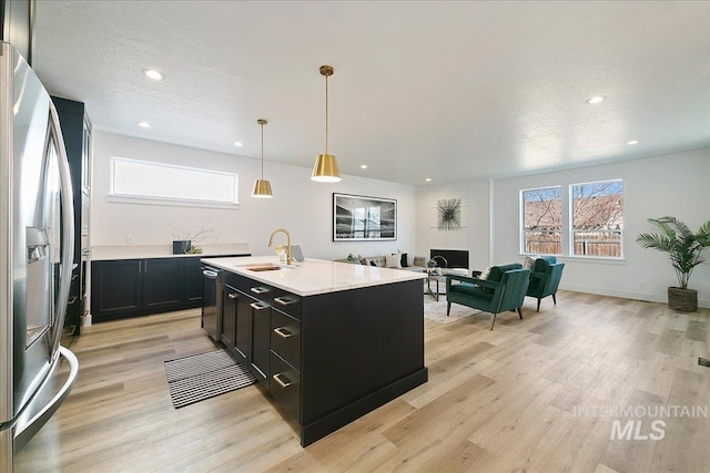 kitchen featuring sink, light stone counters, hanging light fixtures, appliances with stainless steel finishes, and an island with sink