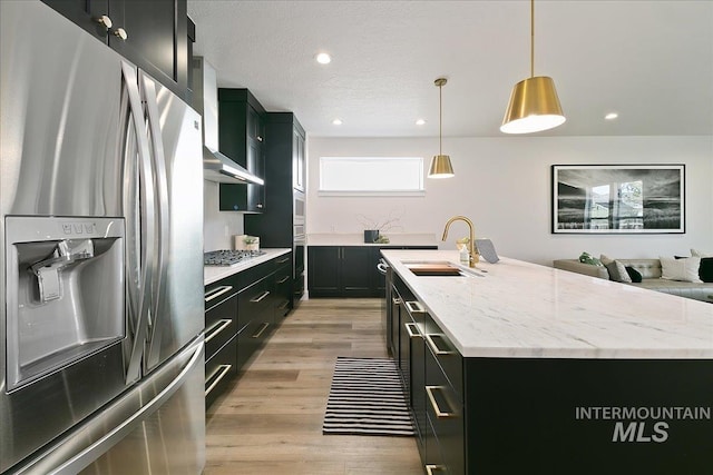 kitchen with sink, hanging light fixtures, stainless steel appliances, a center island with sink, and light wood-type flooring