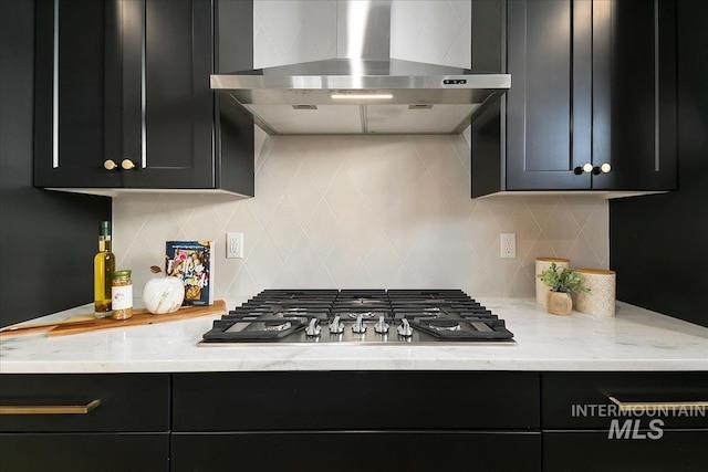 kitchen with stainless steel gas stovetop, backsplash, light stone counters, and wall chimney exhaust hood