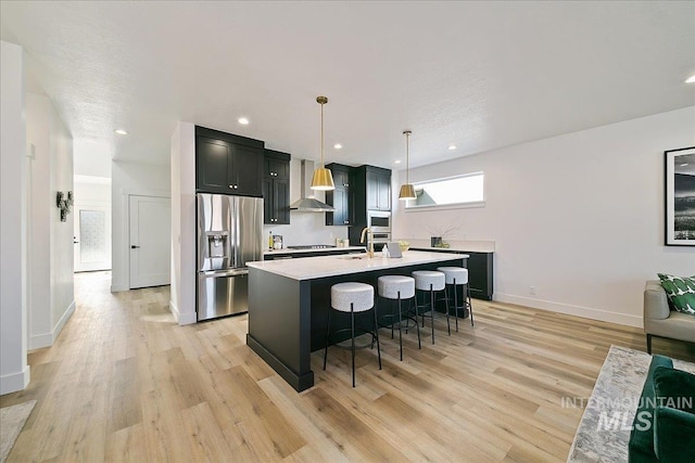 kitchen with a breakfast bar area, hanging light fixtures, a kitchen island with sink, stainless steel refrigerator with ice dispenser, and light hardwood / wood-style flooring