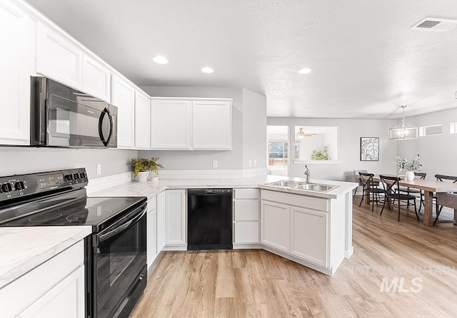 kitchen featuring light wood finished floors, a peninsula, light countertops, black appliances, and a sink