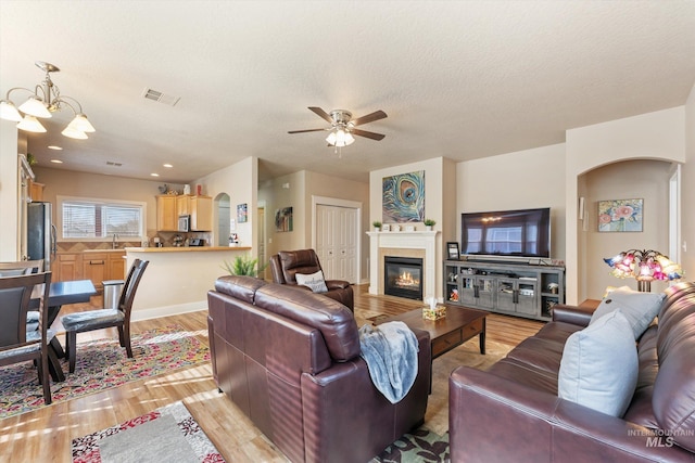 living room featuring light wood-type flooring, visible vents, a textured ceiling, a glass covered fireplace, and arched walkways