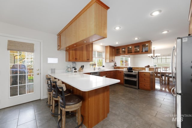 kitchen with an inviting chandelier, light countertops, a peninsula, glass insert cabinets, and stainless steel appliances