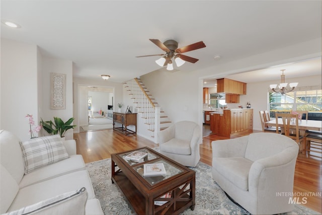 living room with light wood-style flooring, stairway, and ceiling fan with notable chandelier