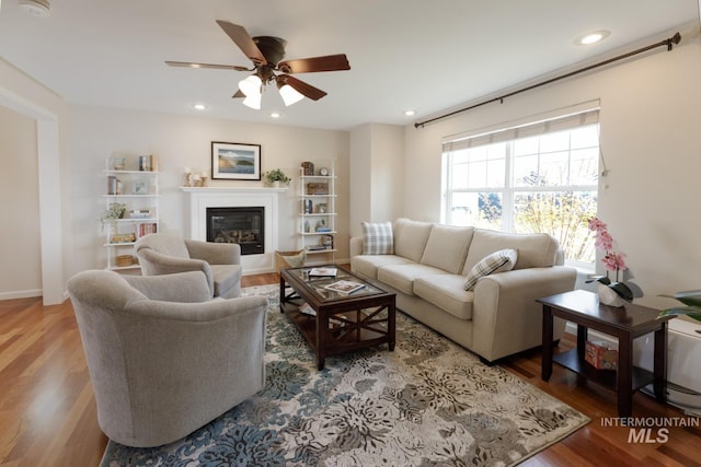 living room featuring a glass covered fireplace, ceiling fan, recessed lighting, and wood finished floors