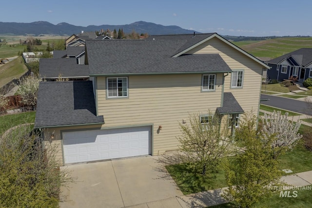 view of side of property with a garage, a mountain view, driveway, and roof with shingles