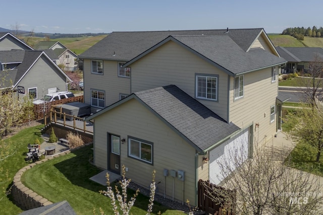 rear view of property featuring a lawn, a residential view, roof with shingles, and a deck