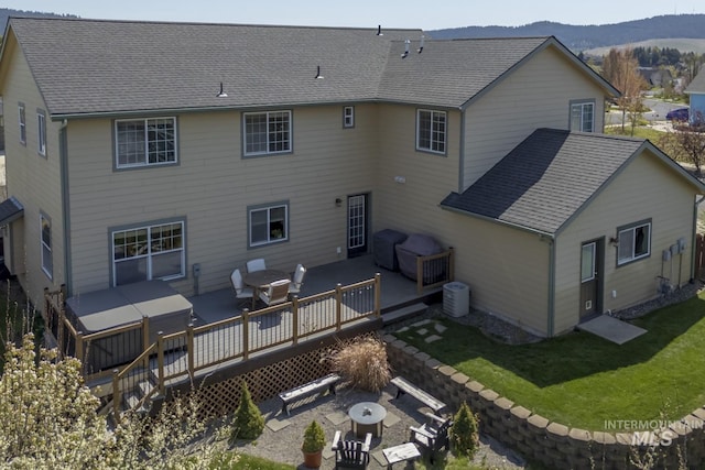 rear view of house with a lawn, a patio, a deck with mountain view, and a shingled roof